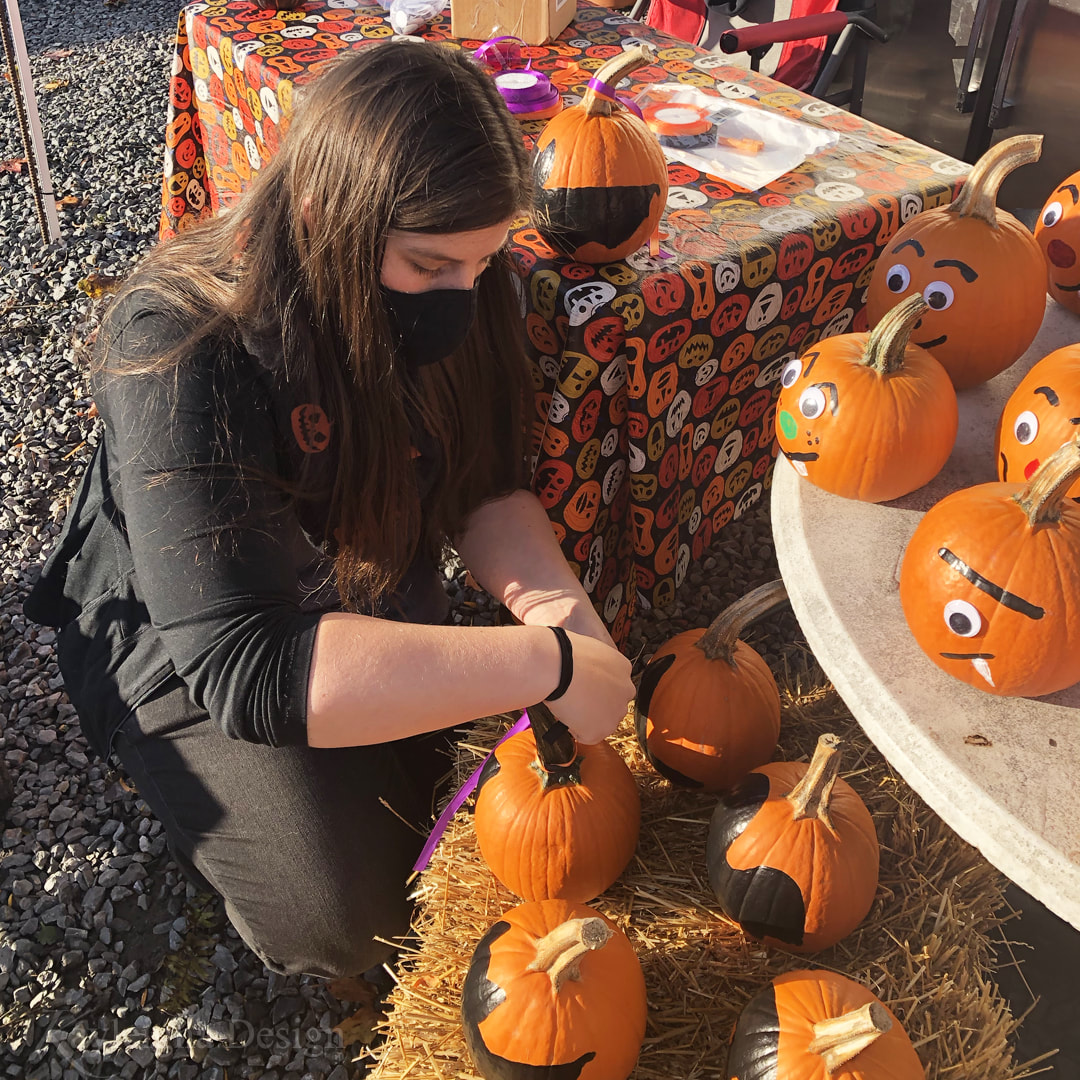 A woman with long brown hair adding ribbons to decorated pumpkins.